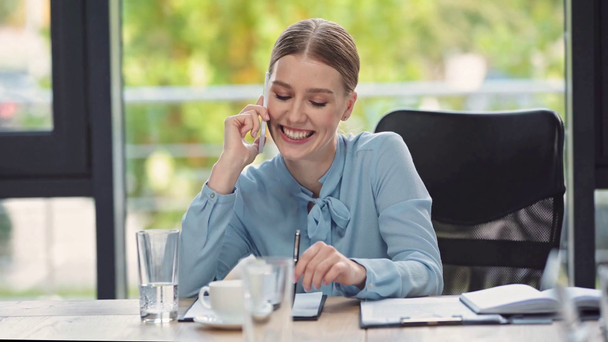 Lächelnde Geschäftsfrau, die am Arbeitsplatz mit dem Smartphone spricht - Filmmaterial, Video