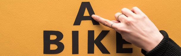 cropped view of woman pointing with finger at bike lettering on orange background - Photo, image