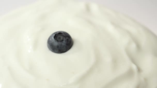 Vers gezond voedsel. Bosbessen vallen in yoghurt op witte achtergrond. Verse vruchten spatten in slagroom. Biologische bes, schoon eten, dieet, vegetarisch, veganistisch voedselconcept. Langzame beweging. - Video