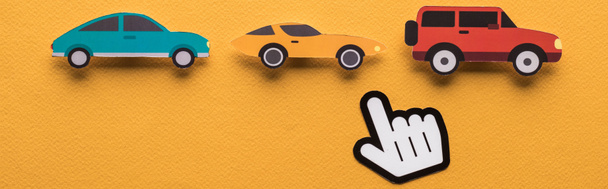 Draufsicht auf Papier geschnittene Autos mit spitzer Hand auf orangefarbenem Hintergrund, Panoramaaufnahme - Foto, Bild