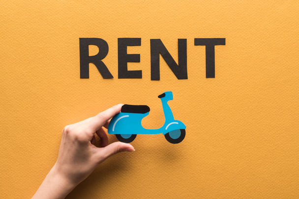 cropped view of woman holding paper cut scooter near rent lettering on orange background - Photo, Image