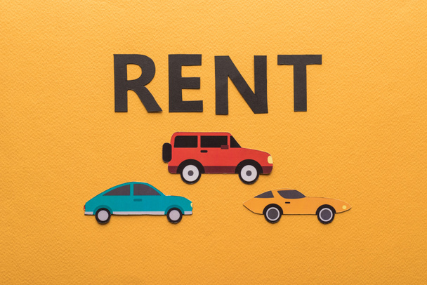 top view of paper cut cars and black rent lettering on orange background - Fotó, kép