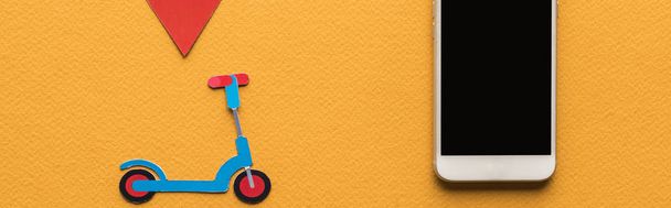 vista superior de patinete de corte de papel, marca de ubicación cerca de teléfono inteligente con pantalla en blanco sobre fondo naranja, tiro panorámico
 - Foto, Imagen