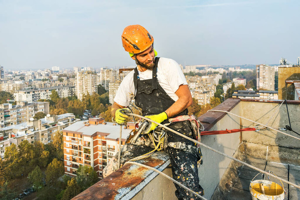 Arbeiter, der an einem Seil hängt, während er die Außenfassade bemalt. industrieller Alpinismus Konzeptbild. Ansicht von oben - Foto, Bild