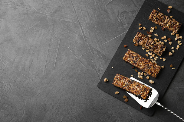 Slate board with healthy granola bars on grey table, top view. Space for text - Фото, изображение