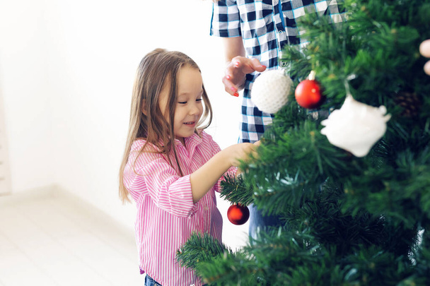 Vacaciones, padres y concepto de celebración - Familia feliz decorando un árbol de Navidad con adornos en la sala de estar sobre fondo blanco
 - Foto, imagen