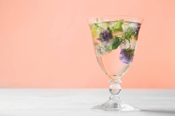 Glass of ice cubes with flowers on light table against pink background. Space for text - Fotó, kép