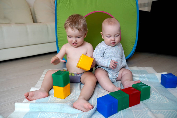 Little children sit on the floor and have fun playing cubes. Chi - Zdjęcie, obraz