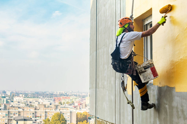 Industrial rope access worker hanging from the building while painting the exterior facade wall. Industrial alpinism concept image. Top view - Photo, Image
