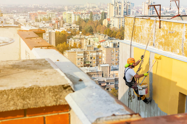 Працівник промислового доступу до мотузки висить з будівлі під час фарбування зовнішньої фасадної стіни. Імідж концепції індустріального альпінізму. Вид зверху
 - Фото, зображення