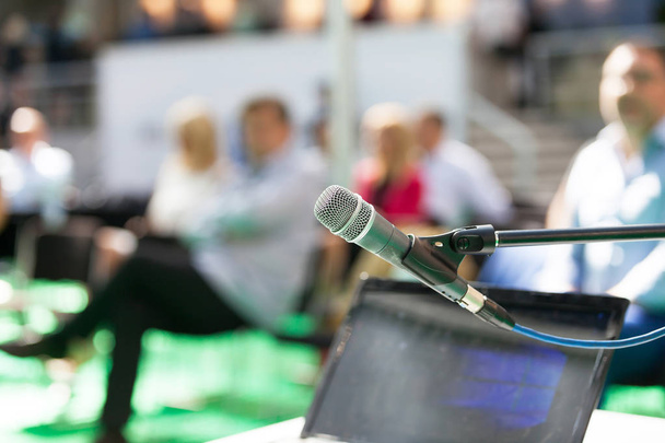 Mikrofon w centrum uwagi przed rozmytymi ludźmi podczas prezentacji biznesowej - Zdjęcie, obraz