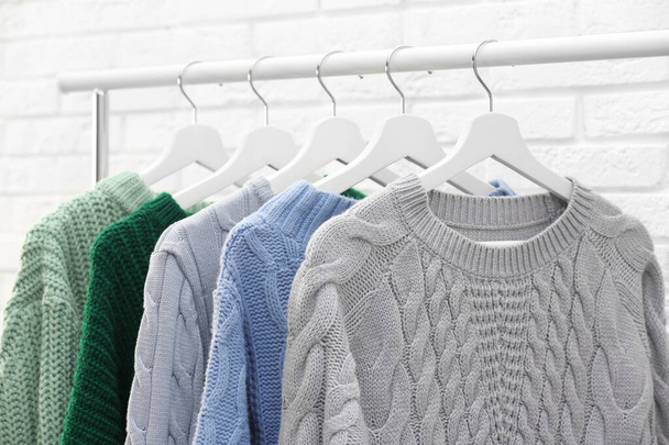 Collection of warm sweaters hanging on rack near brick wall - Zdjęcie, obraz