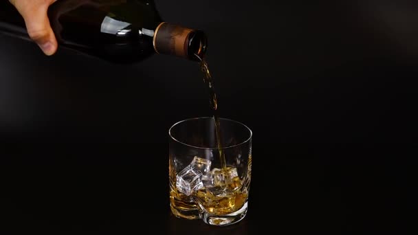 Short film showing whiskey being poured into a tumbler glass with ice on black background. Slow motion. Beautiful backgrounds. Alcohol  - Imágenes, Vídeo