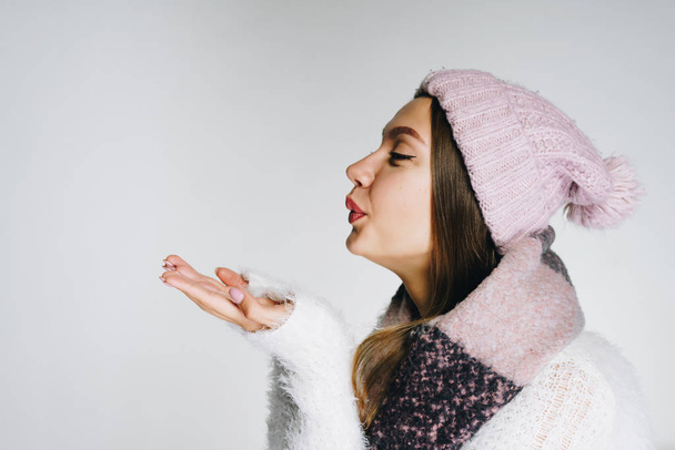 nice girl in warm clothes blowing her hands covering her eyes. studio bright - Foto, Imagen