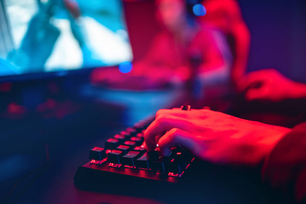 Professional online gamer hand fingers mechanical keyboard in neon color blur background. Soft focus, back view - Foto, afbeelding