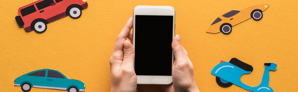 vista ritagliata di donna che tiene smartphone con schermo bianco vicino a macchine di carta su sfondo arancione, colpo panoramico
 - Foto, immagini