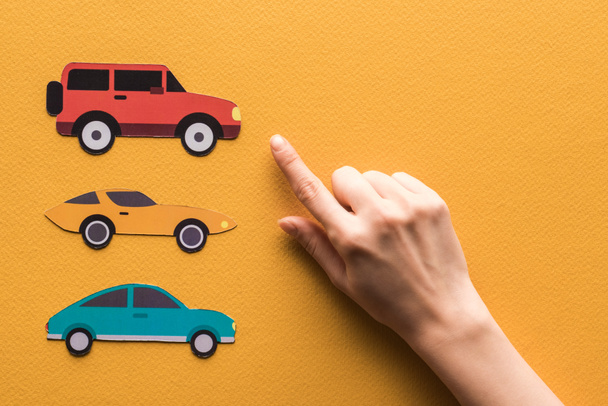 cropped view of woman pointing with finger at paper cars on orange background - Photo, Image