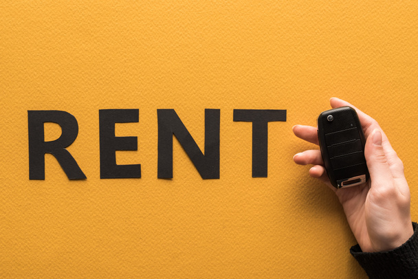 cropped view of woman holding car key near paper cut rent lettering on orange background - Foto, Imagem