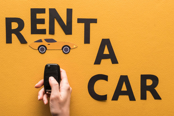cropped view of woman holding key near paper cut rent a car lettering on orange background - Photo, Image