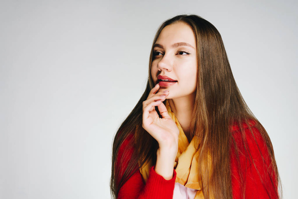a girl with bright lipstick and a red blouse looks with interest and holds her chin with her hand. bright studio - Foto, Bild