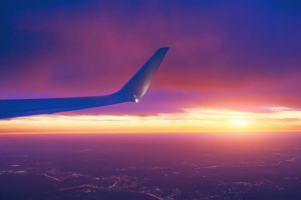 Naplemente ég egy repülőgép oldalsó szárny kilátás nyílik a horizont és a városi fények. - Fotó, kép
