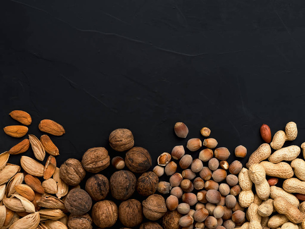 Natural organic nuts, almonds, peanuts, walnuts and hazelnuts on a black background. View from above. The concept of a healthy diet, natural antioxidants. Natural light. Food background, copy space. - Photo, Image