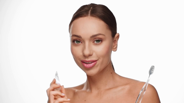uśmiechnięta kobieta trzymająca szczoteczkę do zębów i pastę do zębów wyizolowaną na białym - Materiał filmowy, wideo