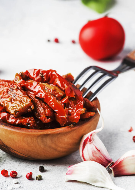 Sun dried tomatoes in olive oil with green basil and spices in wooden bowl on gray kitchen table, place for text - Fotografie, Obrázek