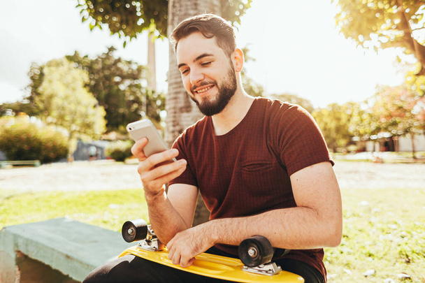 Young skater man using smartphone in the park - Photo, Image