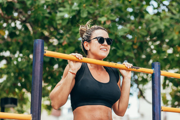 Athletic woman doing pull ups in public park - Photo, image