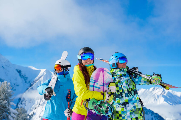 Due uomini e donne con snowboard e sci che guardano in direzioni diverse in piedi sulla neve resort sullo sfondo di montagna e cielo nuvoloso
 . - Foto, immagini