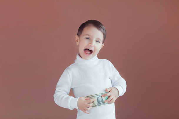 mały chłopiec trzyma w rękach dolara na różowym tle, radość z pierwszych zarobków, dobry wkład do dziecka na przyszłość - Zdjęcie, obraz