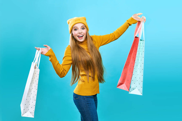 Fashionista girl with bags. Young brunette woman with purchases. Joyful beauty was on sale, on a blue background. Concept of sale, discounts, black friday. - Photo, Image