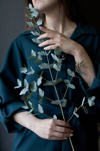 Portrait of a girl in a green dress holding a eucalyptus branch on a dark background, selective focus - Photo, Image