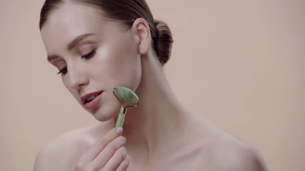 mujer desnuda usando rodillo de jade aislado en beige
 - Imágenes, Vídeo