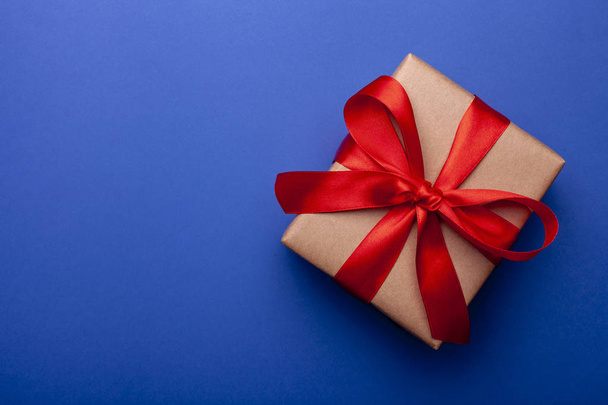 schöne Weihnachtsgeschenkschachtel in Bastelpapier mit roter Schleife auf farbigem Hintergrund verpackt. Gegenwart auf blauem Hintergrund mit Platz für Text. Ansicht von oben - Foto, Bild