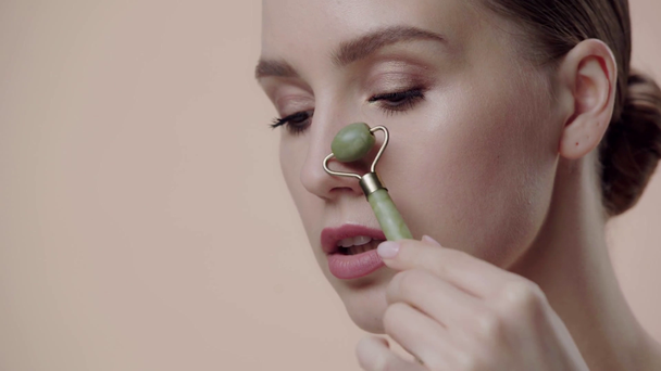 close up of girl using jade roller isolated on beige  - Filmati, video