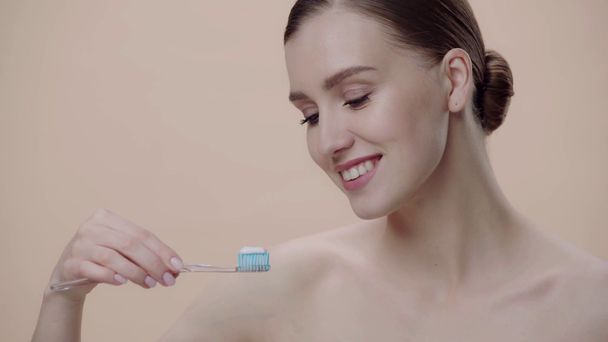 γυμνό κορίτσι κρατώντας οδοντόβουρτσα απομονωμένη σε μπεζ  - Πλάνα, βίντεο