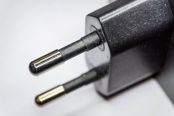 Close-up de preto dois pólos redondo-pino 230V AC fonte de alimentação europlug com pino banhado em foco parcial un fundo isolado branco
 - Foto, Imagem