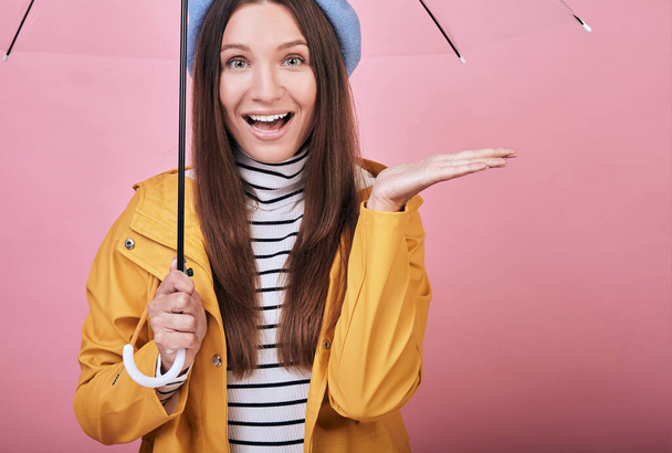 Happy cheerful girl in striped blouse and yellow rain jacket with umbrella in hand - Photo, Image