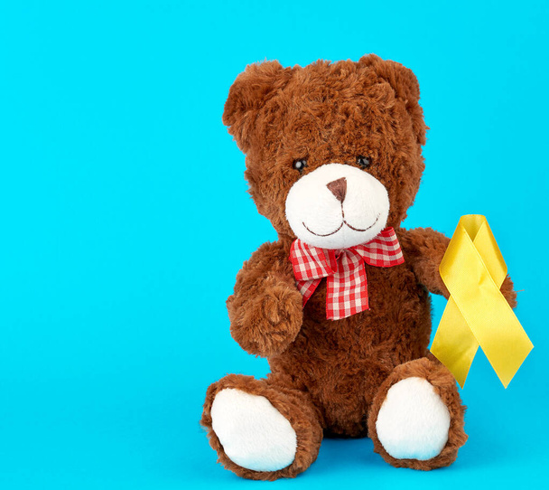 bruine teddybeer zit en houdt in zijn poot een geel zijden lint  - Foto, afbeelding