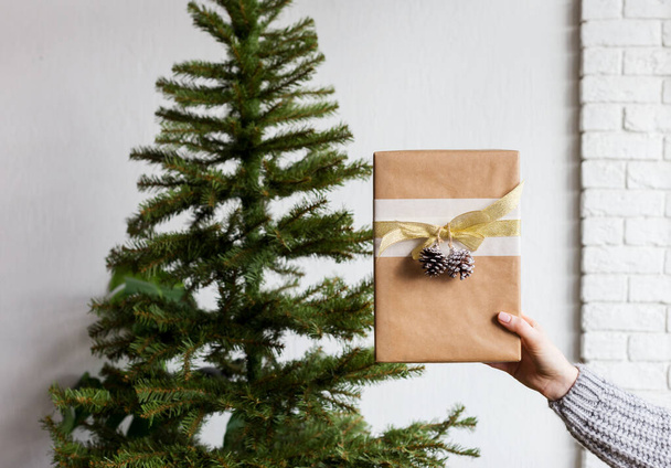 Gift box in woman's hand and christmas tree behind - Foto, afbeelding