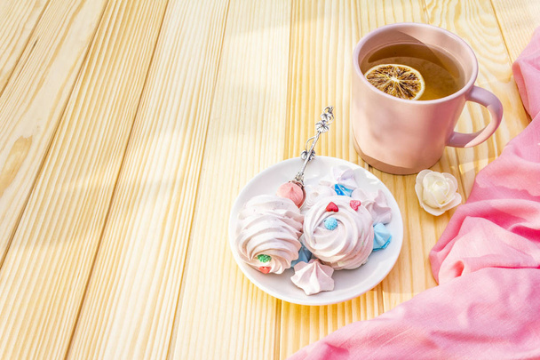 Conceito romântico de pequeno-almoço doce. Chá verde, limão, merengue (bolo). Em fundo de madeira com pano rosa
. - Foto, Imagem
