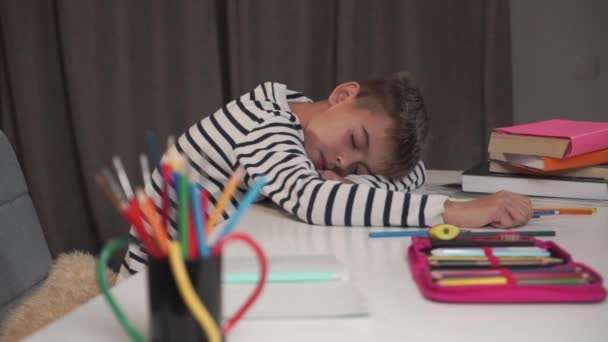 Nahaufnahme eines kleinen kaukasischen Jungen, der am Tisch schläft. Schüler müde nach Hausaufgaben zu Hause. Niedliches Kind in gestreifter Jacke nach dem Studium erschöpft. - Filmmaterial, Video