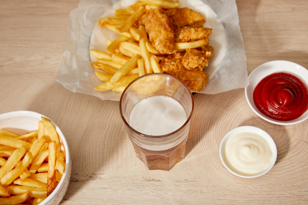 glass of beer, chicken nuggets with french fries, ketchup and mayonnaise on wooden table - Zdjęcie, obraz