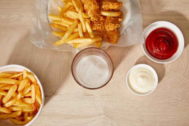 top view of glass of beer, chicken nuggets with french fries, ketchup and mayonnaise on wooden table - Photo, Image