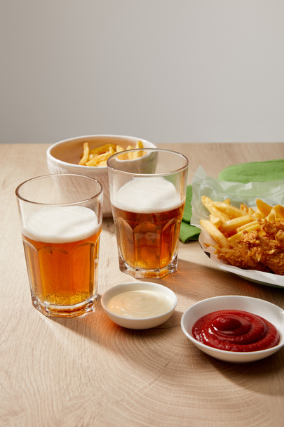 copos de cerveja, nuggets de frango com batatas fritas, ketchup e maionese em mesa de madeira em fundo cinza
 - Foto, Imagem