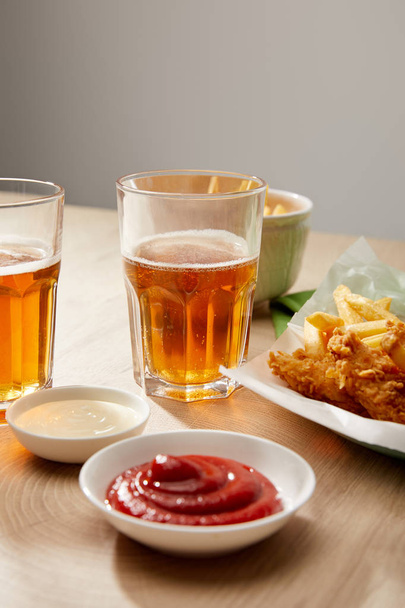 ビール、フライドポテトとチキンナゲット、ケチャップとマヨネーズのグレーの背景に木製のテーブルの上 - 写真・画像