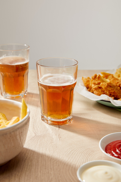 lasilliset olutta, kananugetteja ranskalaisilla perunoilla, ketsuppia ja majoneesia puupöydällä harmaalla pohjalla
 - Valokuva, kuva