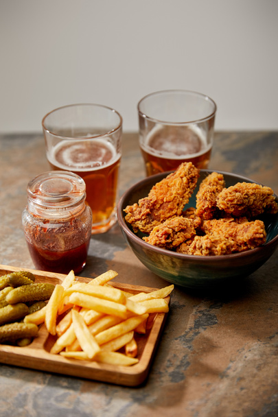 delicious chicken nuggets, french fries and gherkins near glasses of beer on stone surface isolated on grey - Fotografie, Obrázek